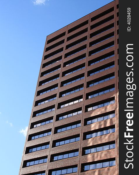 A brown brick skyscraper with rectangular windows and a bright blue sky.