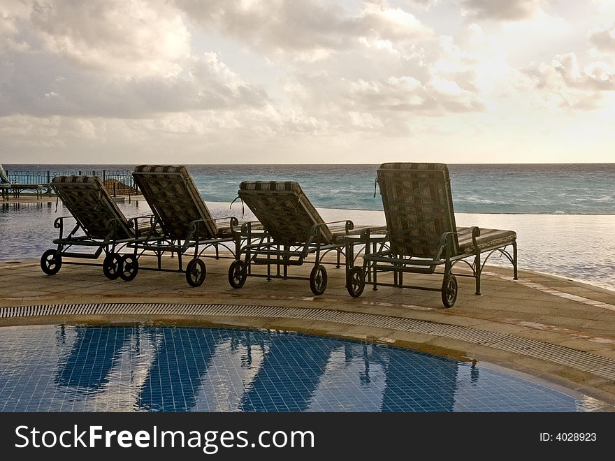 Four chaise lounges between pool and ocean facing the sea at sunrise. Four chaise lounges between pool and ocean facing the sea at sunrise