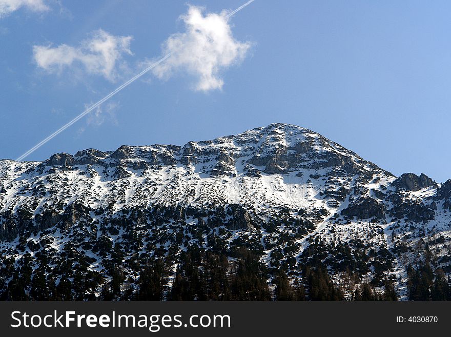 Alpes, Bavaria, Germany -Not so far from  Inzell City .Peak of Zwisel Mountain at the background of sky clouds and airplane track. Alpes, Bavaria, Germany -Not so far from  Inzell City .Peak of Zwisel Mountain at the background of sky clouds and airplane track.