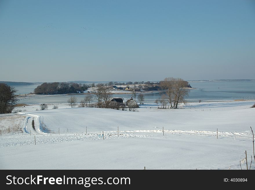 Idylic winter landscape with, fram, fields and frozen sea.