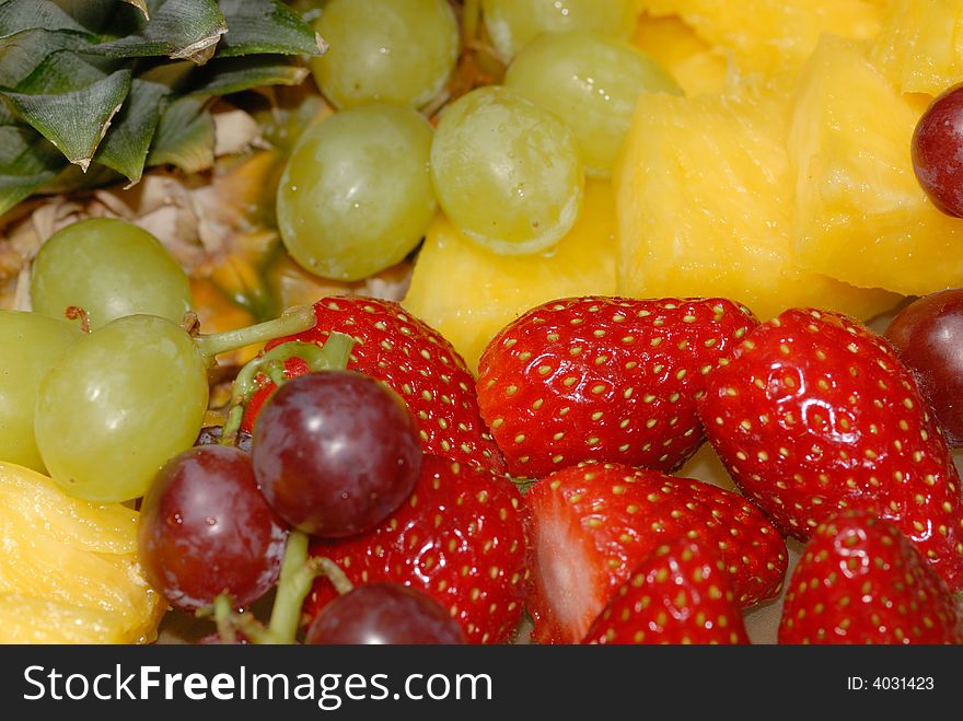 Refreshing fruit salad with pineapple, red and green grapes and strawberries - close detail