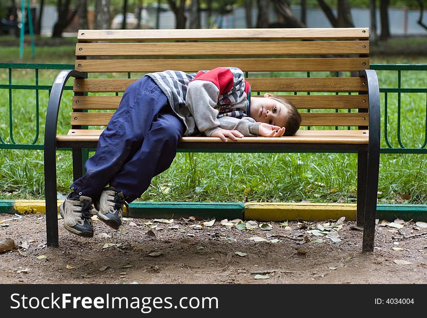 The little boy has sat down on a bench to have a rest. The little boy has sat down on a bench to have a rest