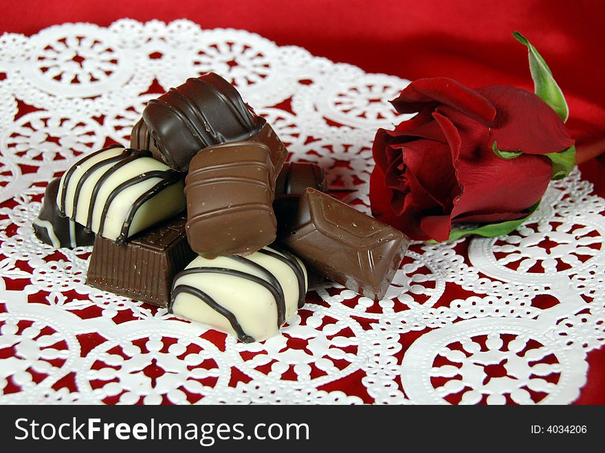 Single red rose with fancy chocolates on a lace paper doily. Single red rose with fancy chocolates on a lace paper doily.