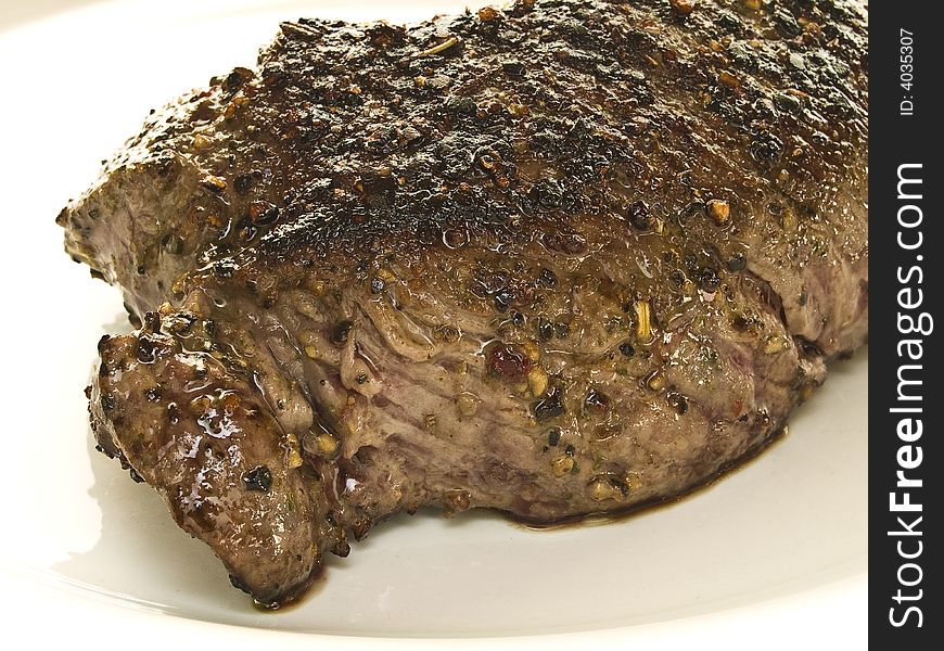 Piece of beef steak spiced with black pepper on a white plate. Piece of beef steak spiced with black pepper on a white plate