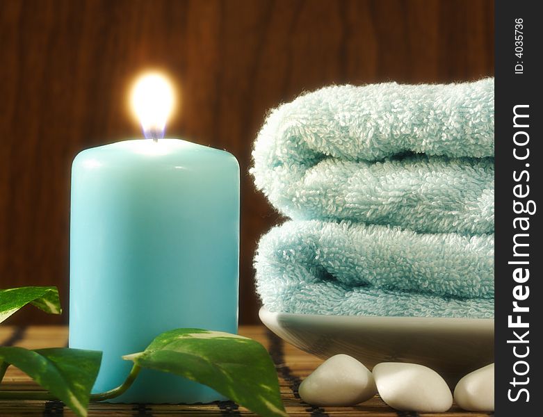 Blue towel and candle, green leaf and a few white stones in front of wood background. Blue towel and candle, green leaf and a few white stones in front of wood background