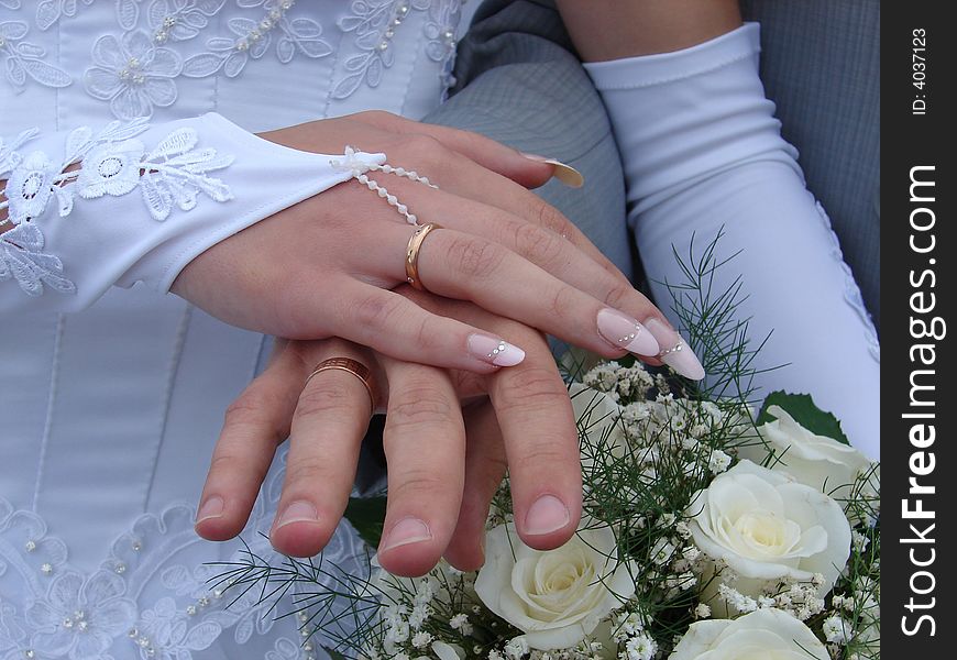Hand of the groom and the bride with wedding rings and a bouquet of white roses. Hand of the groom and the bride with wedding rings and a bouquet of white roses