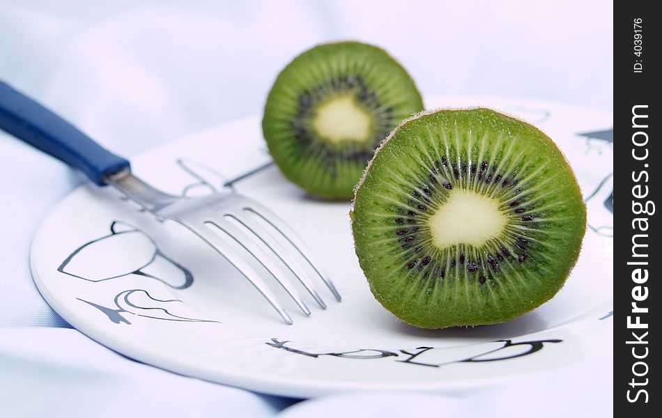 Two kiwis and a fork on a plate. Two kiwis and a fork on a plate