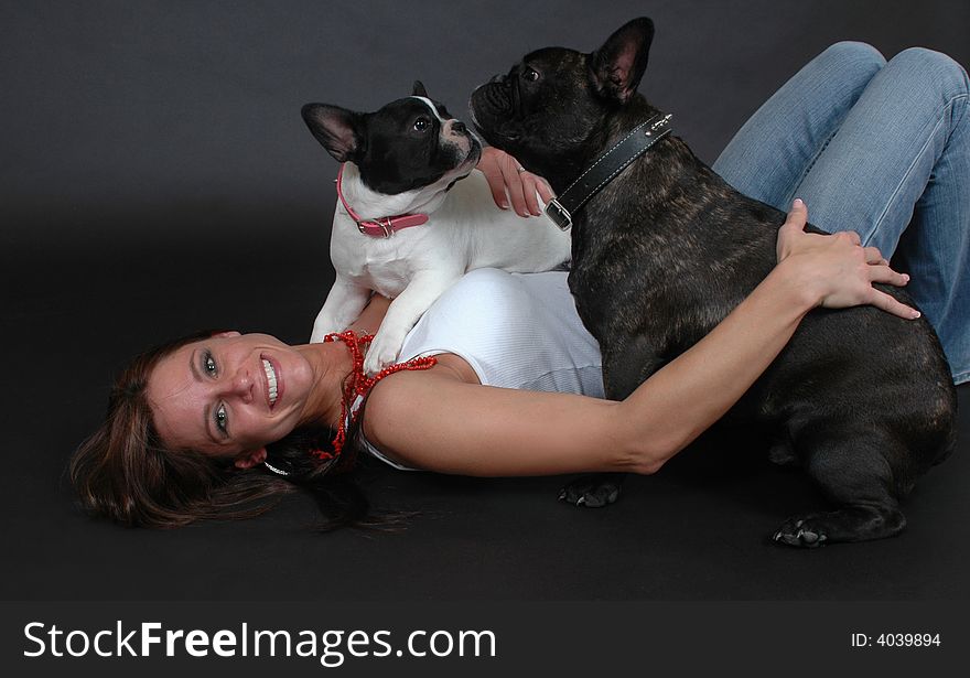 Woman holding her French Bull dogs on black background. Woman laying on floor. Woman holding her French Bull dogs on black background. Woman laying on floor.