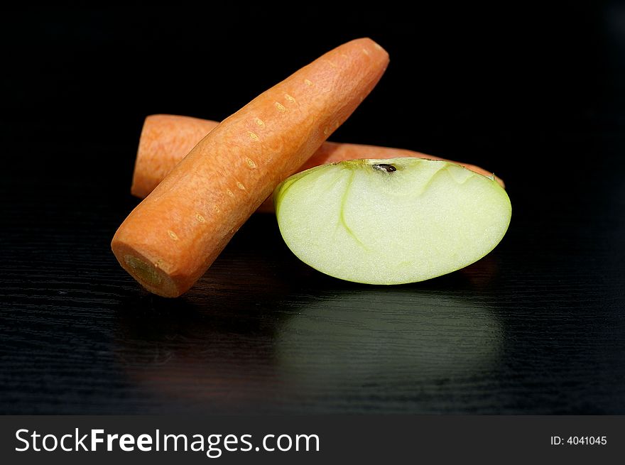 two carrots and the slice of apple against the black background. two carrots and the slice of apple against the black background