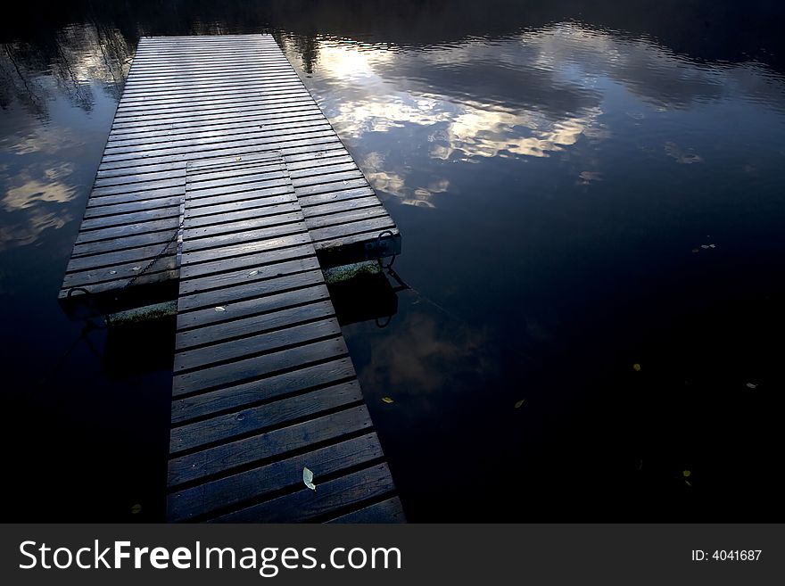 Abandoned wooden pier at sunset with cloud reflexes in the water