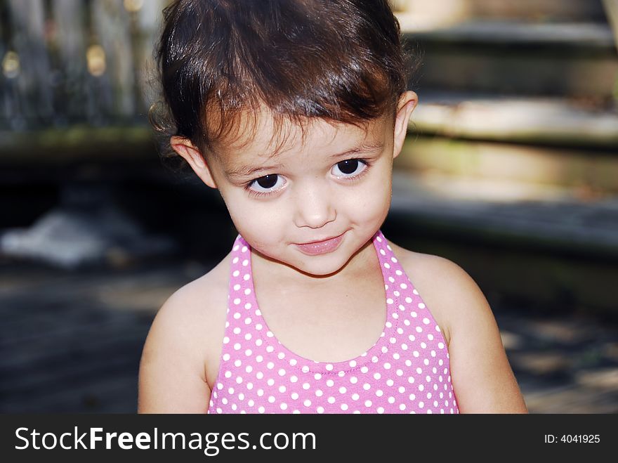 Cute little baby girl giving a look of sweetness wearing a pink polka dot halter dress.  She has big brown eyes and brunette hair with a redish tint.