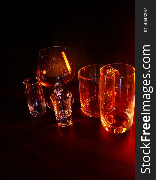 Glasses, wineglasses and a cup on a black background, specks of light, evening light