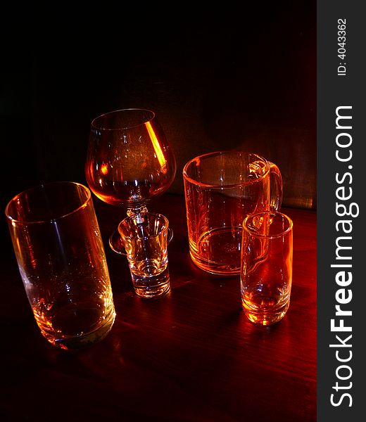 Glasses, wineglasses and a cup on a black background, specks of light, evening light