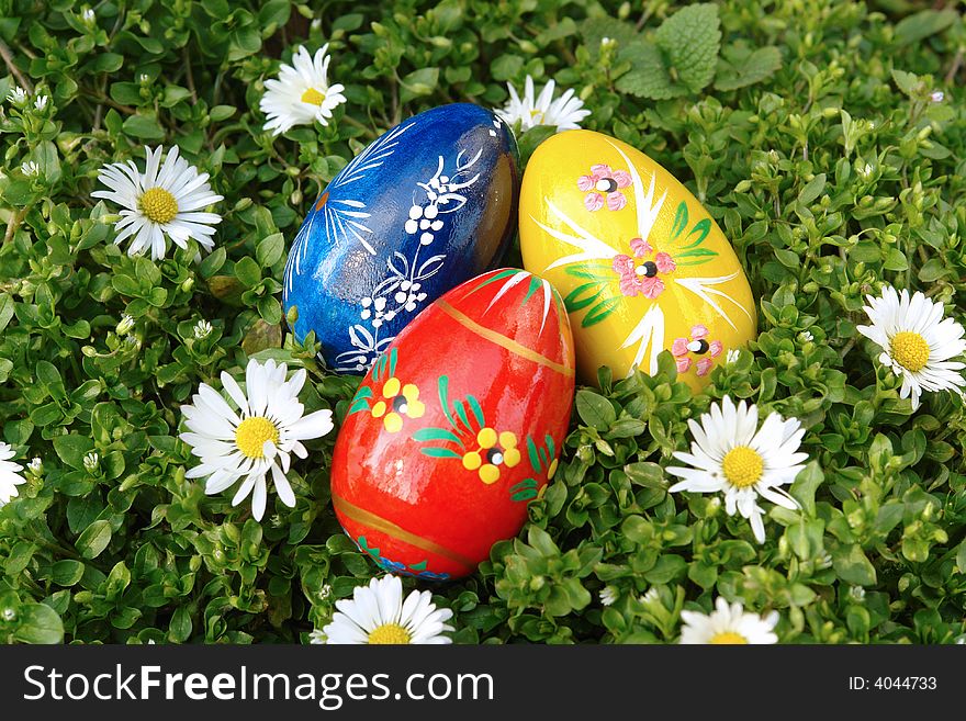 Three painted easter eggs in grass with daisies