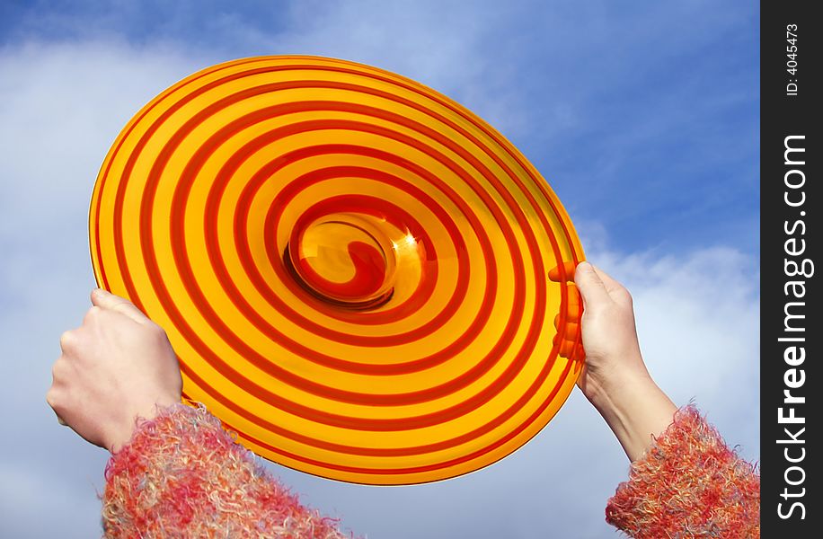 Red the and orange disc in the girl's palms on background of blue sky. Red the and orange disc in the girl's palms on background of blue sky