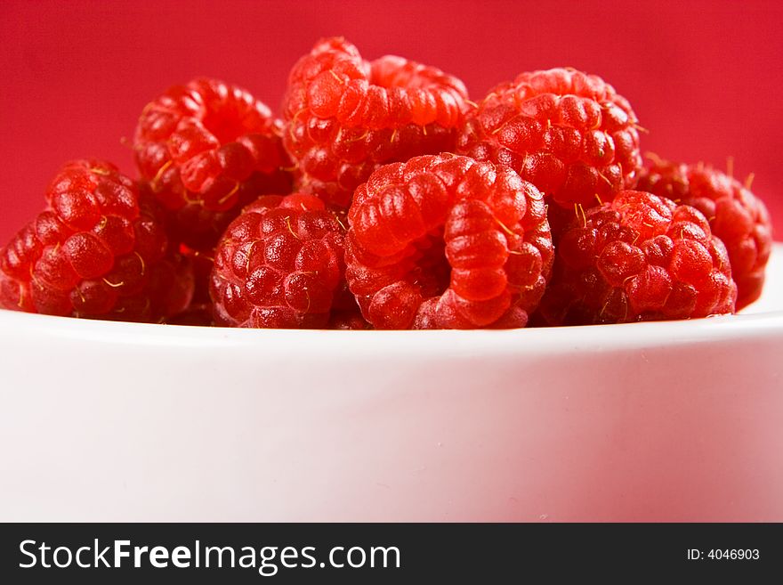 A dish of raspberries on a red background. A dish of raspberries on a red background