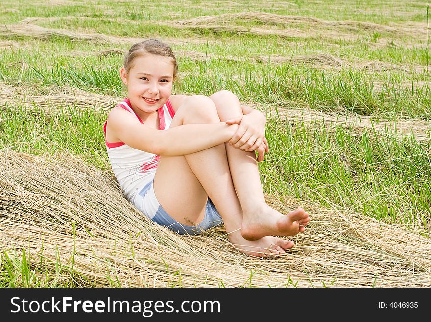 A pretty girl sitting in a field with cut grass