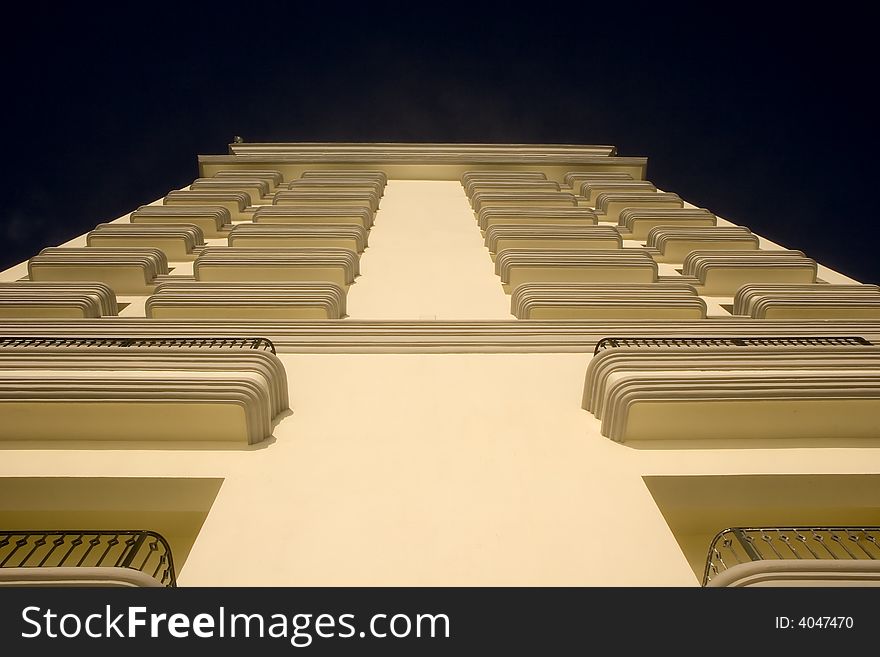 A white building from below with balconies into the blue sky. A white building from below with balconies into the blue sky