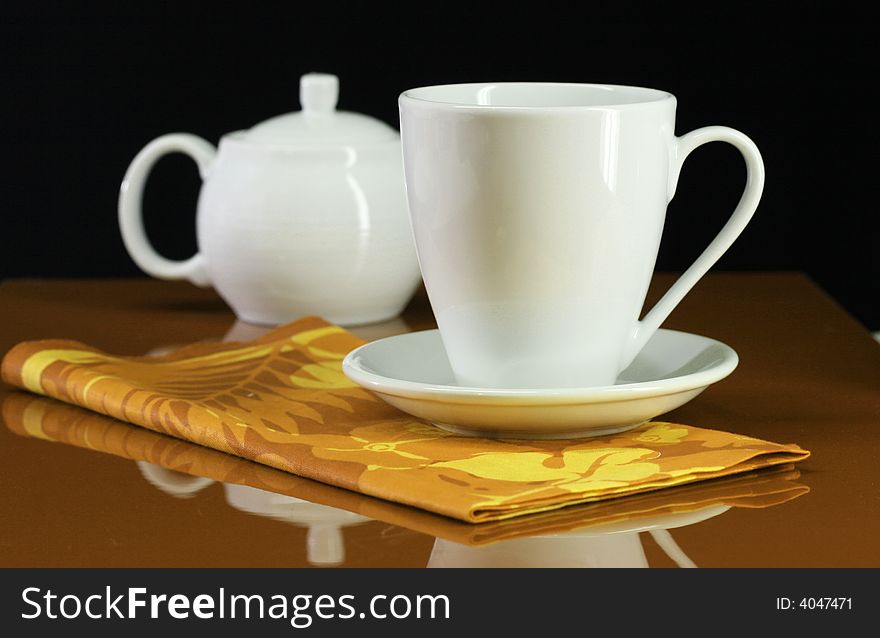A coffee cup and teapot set on an orange table. A coffee cup and teapot set on an orange table