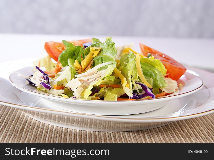 Healthy salad with lettuce, carrots, radish, cabbage, turkey, tomato wedges, and cheese