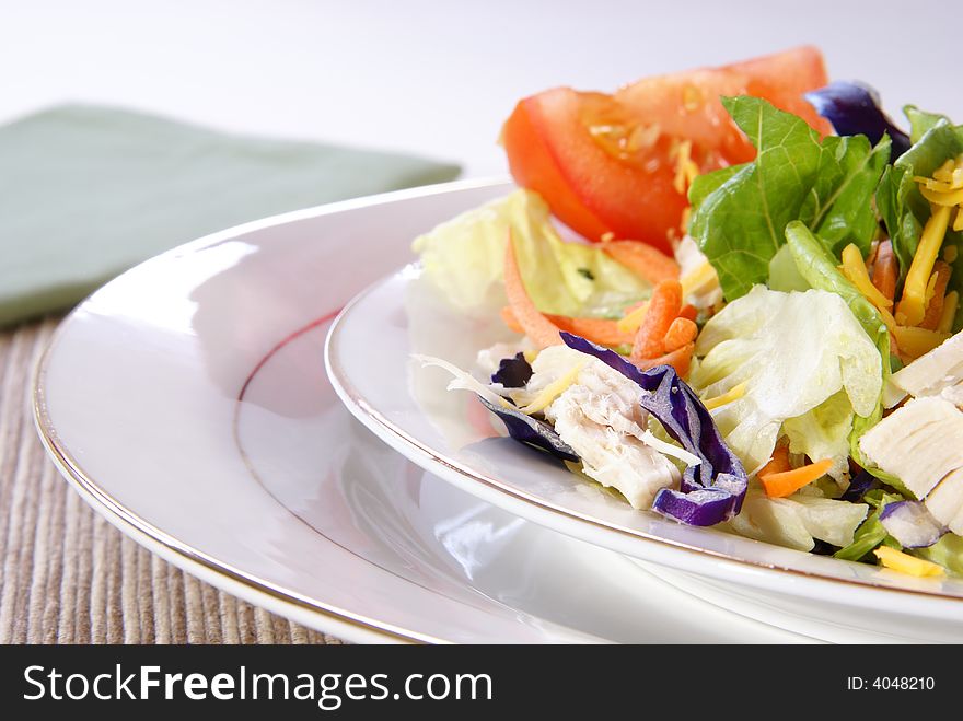 Healthy salad with lettuce, carrots, radish, cabbage, turkey, tomato wedges, and cheese