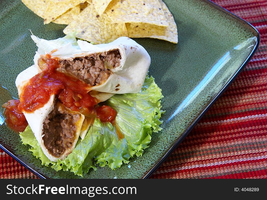 Homemade burrito with beef, beans, cheese, salsa, tortillas, chilis, and corn chips.