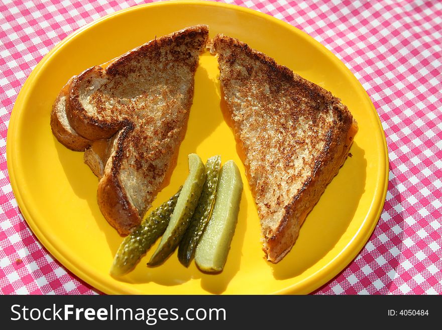 Grilled cheese sandwich on a yellow plate with pickles. Grilled cheese sandwich on a yellow plate with pickles