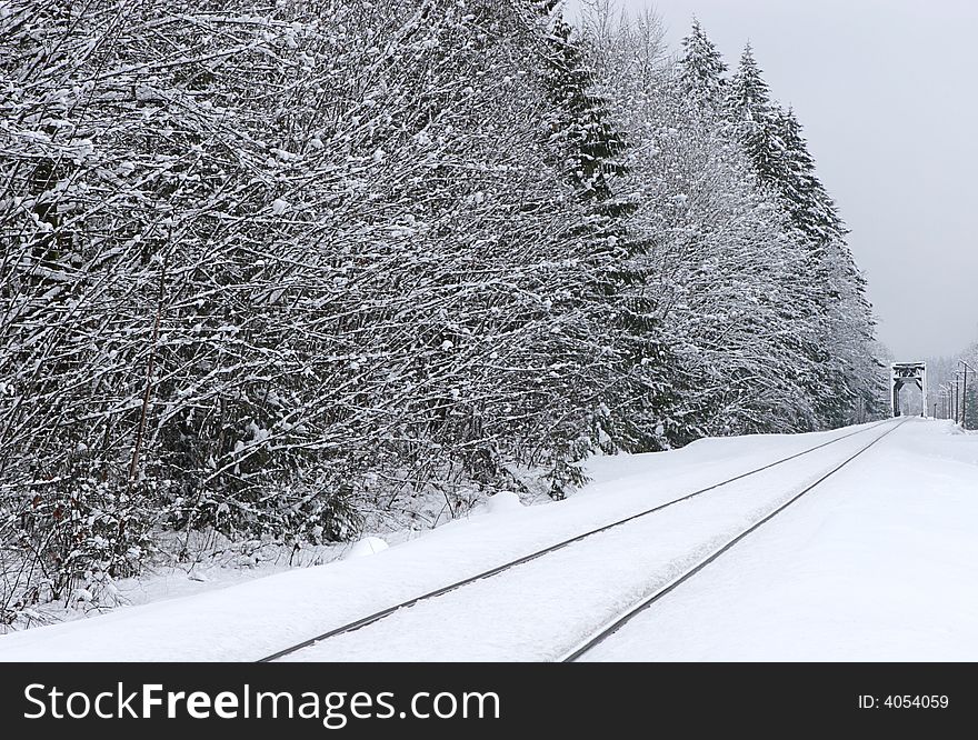 Rural winter scene of Railroad tracks and trees with bridge in background, covered in snow. Rural winter scene of Railroad tracks and trees with bridge in background, covered in snow