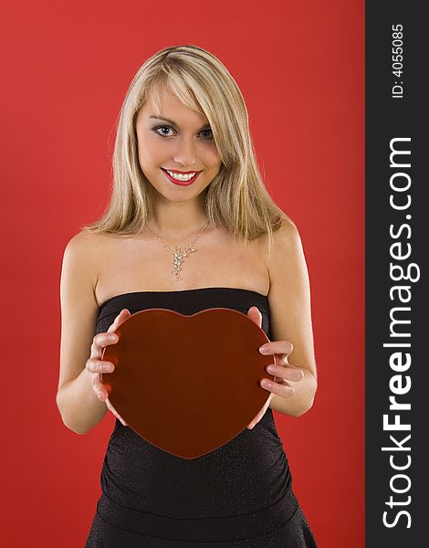Beautiful woman in black dress, holding heart-shaped box of chocolates. Smiling and looking at camera. Front view. Beautiful woman in black dress, holding heart-shaped box of chocolates. Smiling and looking at camera. Front view