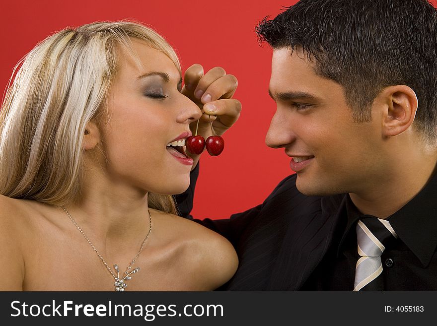 Young enamoured couple. Man is feeding woman by cherry and smiling. Young enamoured couple. Man is feeding woman by cherry and smiling