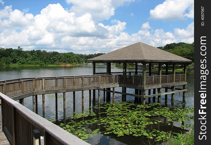 A gazebo and boardwalk on wooden stilts in the middle of a lake surrounded by lily pads. A gazebo and boardwalk on wooden stilts in the middle of a lake surrounded by lily pads