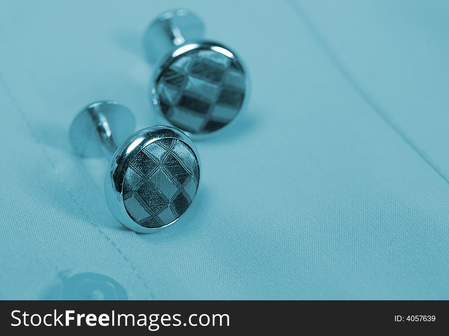 Pair of cuff links on a shirt with a blue tint. Pair of cuff links on a shirt with a blue tint