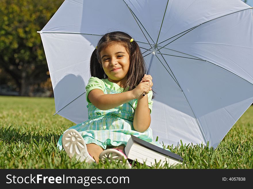 Little girl playing with a white umbrella and book on the ground. Little girl playing with a white umbrella and book on the ground