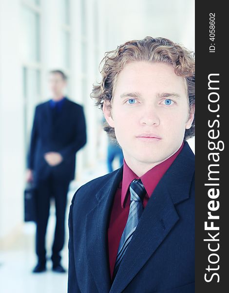 Two businessmen in hallway, one with a briefcase, the other with very blue eyes