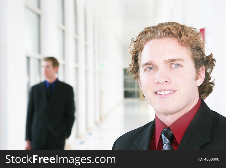 Two businessmen in hallway, one pauses to smile