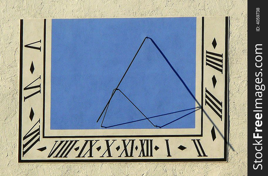 A blue sundial with Roman numerals. The tim it shows is quater to three.