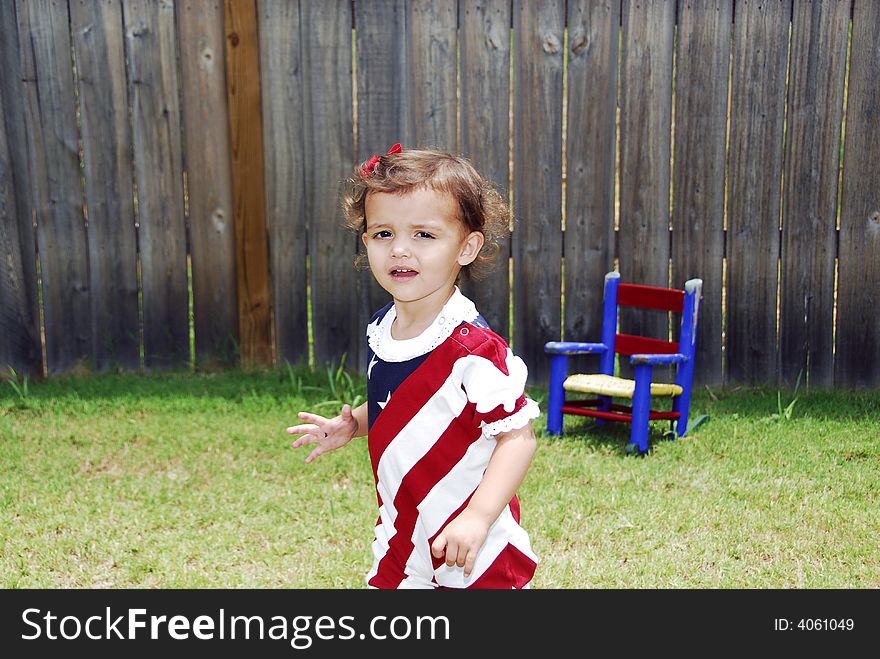 Cute baby girl dressed in her red, white, and blue outfit with her red and blue rocker in the background. Cute baby girl dressed in her red, white, and blue outfit with her red and blue rocker in the background.