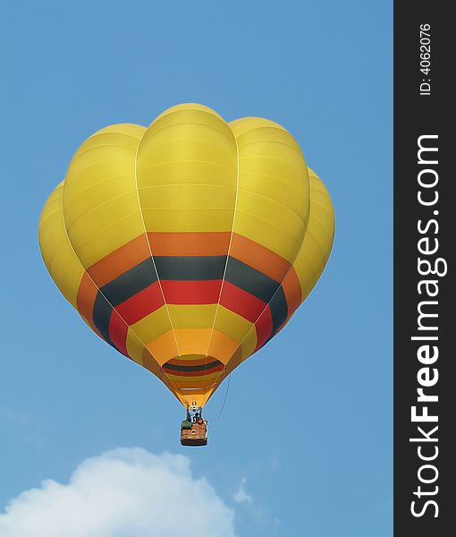 Yellow hot-air balloon flying mid-air. Blue sky background.