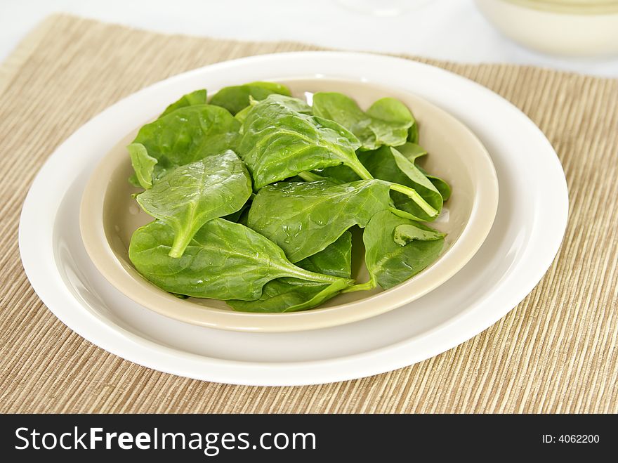 Fresh raw spinach leaves on a plate with placemat. Low DOF.