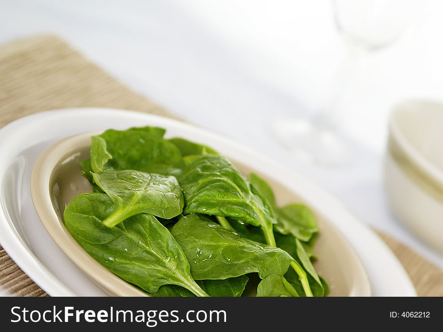 Fresh raw spinach leaves on a plate with placemat. Low DOF.