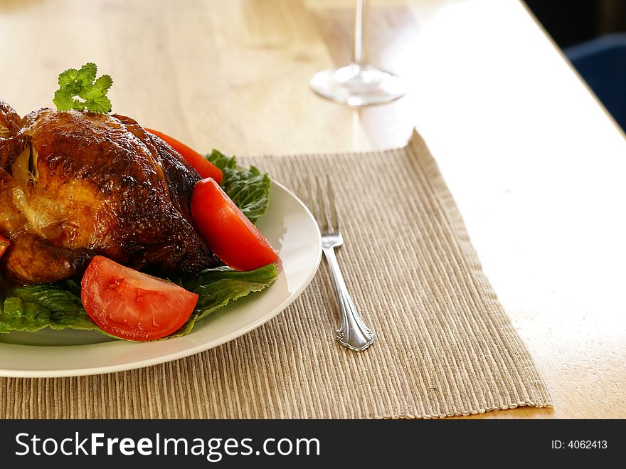 Whole roasted chicken on bed of lettuce with tomatoe wedges.