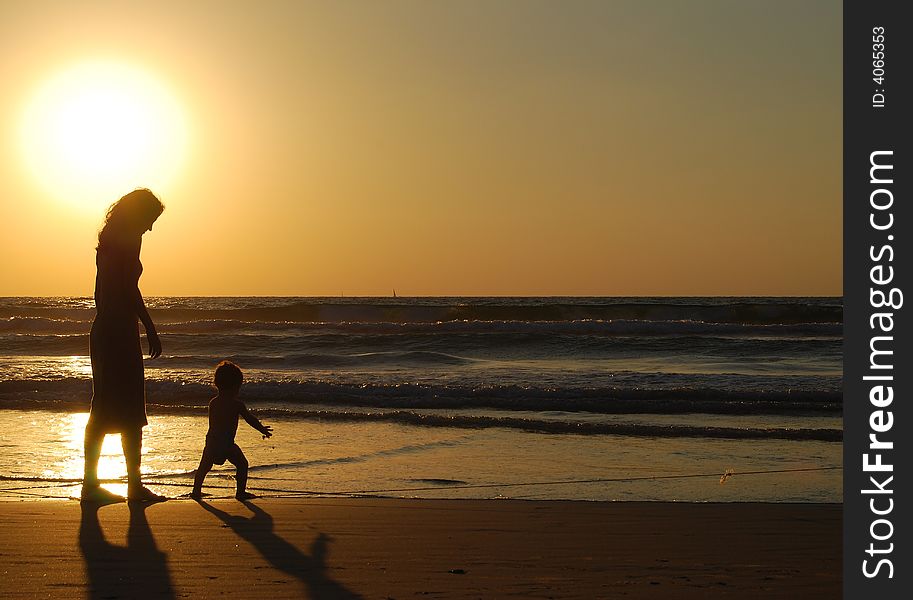 Young woman with small child on the sea shore on sunset