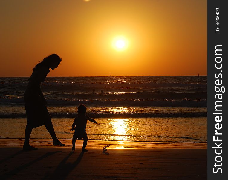 Young woman with small child on the sea shore on sunset