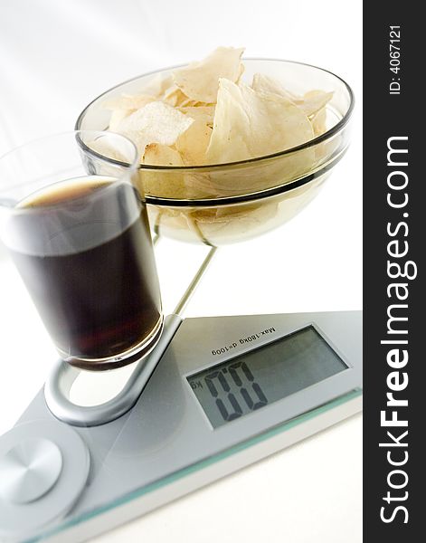 Glass of diet cola and „diet chips” on the electronic balance showing 0.0kg, methaphore of light food. Glass of diet cola and „diet chips” on the electronic balance showing 0.0kg, methaphore of light food