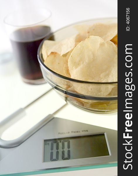 Glass of diet cola and â€ždiet chipsâ€ on the electronic balance showing 0.0kg, methaphore of light food. Glass of diet cola and â€ždiet chipsâ€ on the electronic balance showing 0.0kg, methaphore of light food