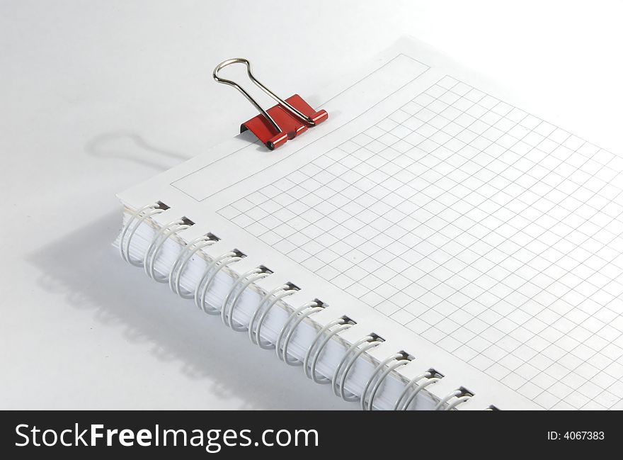 White notebook and red paperclip on white surface