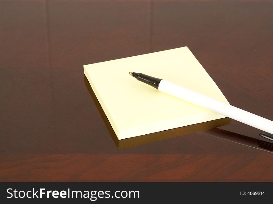 Yellow square notepad and pen on dark wood desk