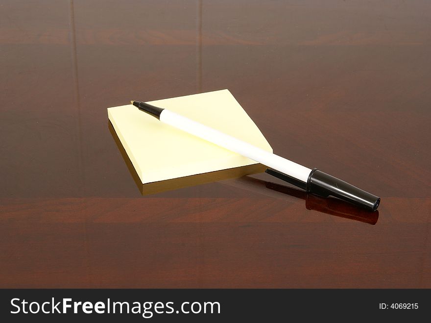 Yellow square notepad and pen on dark wood desk