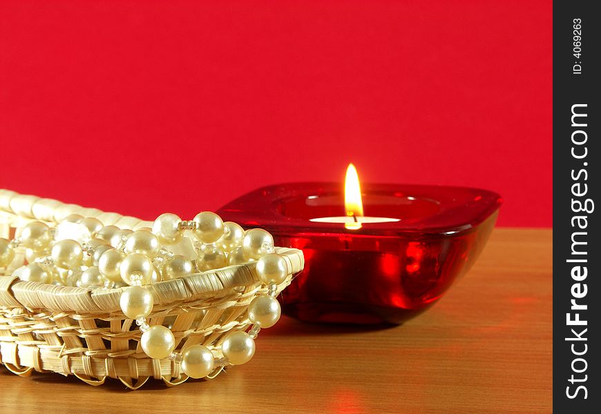 The candle and pearls on the table. Red background. The candle and pearls on the table. Red background.