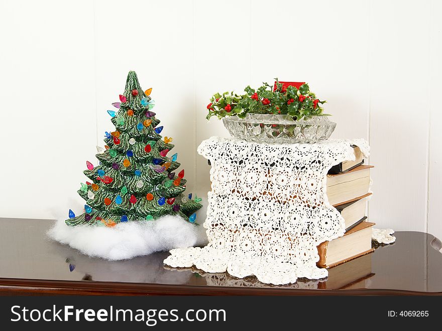 Christmas Decor. Handmade porcelain tree next to books with antique doily and holiday greenery in crystal cut dish.